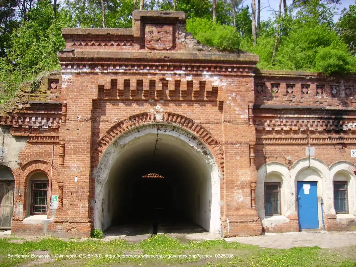 Wejście do tunelu w ceglanej twierdzy Osowiec. Zarośnięte zielenią mury i łukowate przejście.