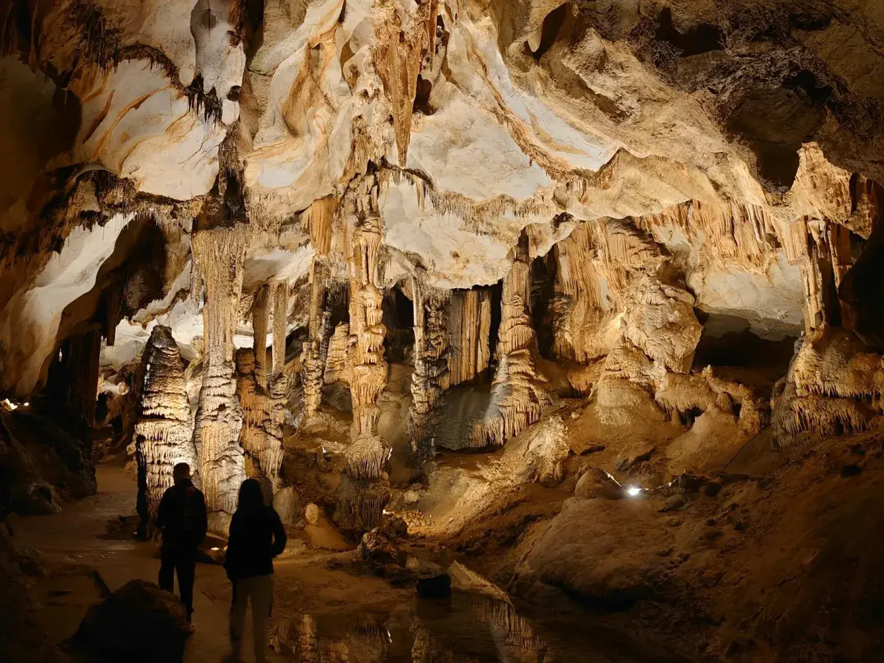 Dwie osoby zwiedzają imponujące jaskinie w Polsce, podziwiając stalaktyty i stalagmity.