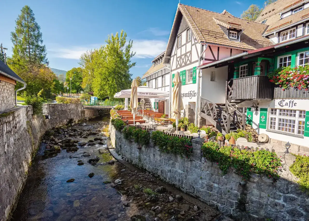 Urokliwy deptak w Szklarskiej Porębie nad kamienistym potokiem, z kawiarnią i restauracją z ogródkiem.