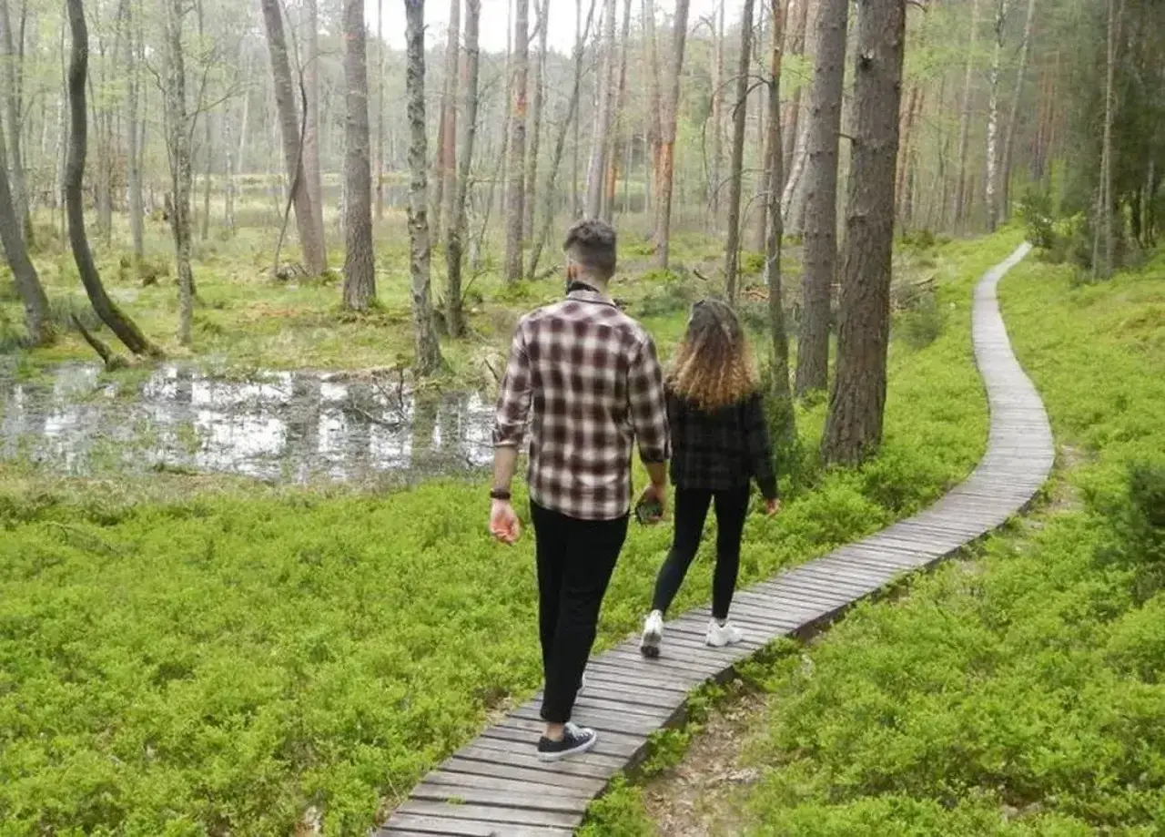 Para spaceruje drewnianą kładką przez malowniczy las. Odkrywają magiczne miejsca kujawsko-pomorskie, gdzie natura zachwyca zielenią i spokojem.