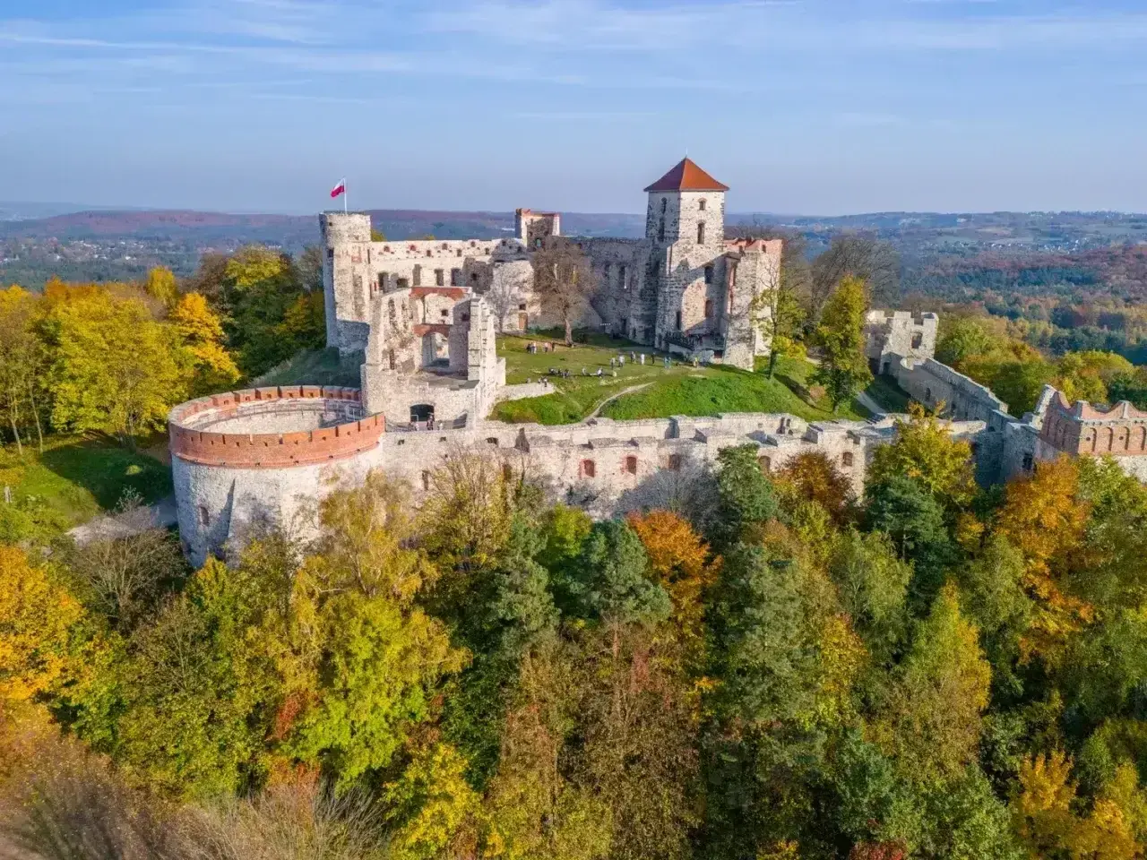 Ruiny zamków Orlich Gniazd na wzgórzu, otoczone jesiennym lasem. Polska flaga powiewa na wieży.