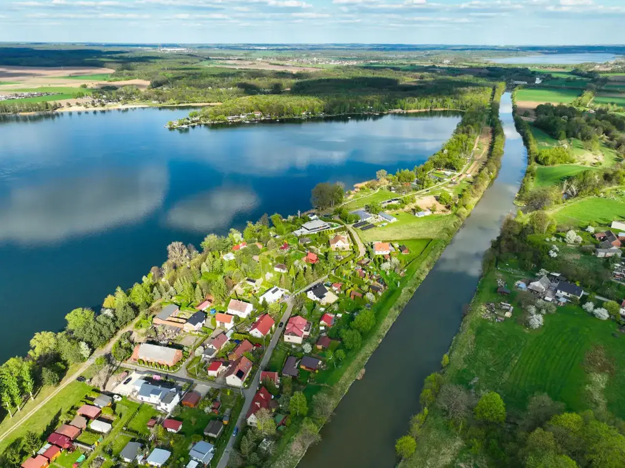Malownicze jezioro Pławniowice z kanałem i zabudowaniami w otoczeniu zieleni.