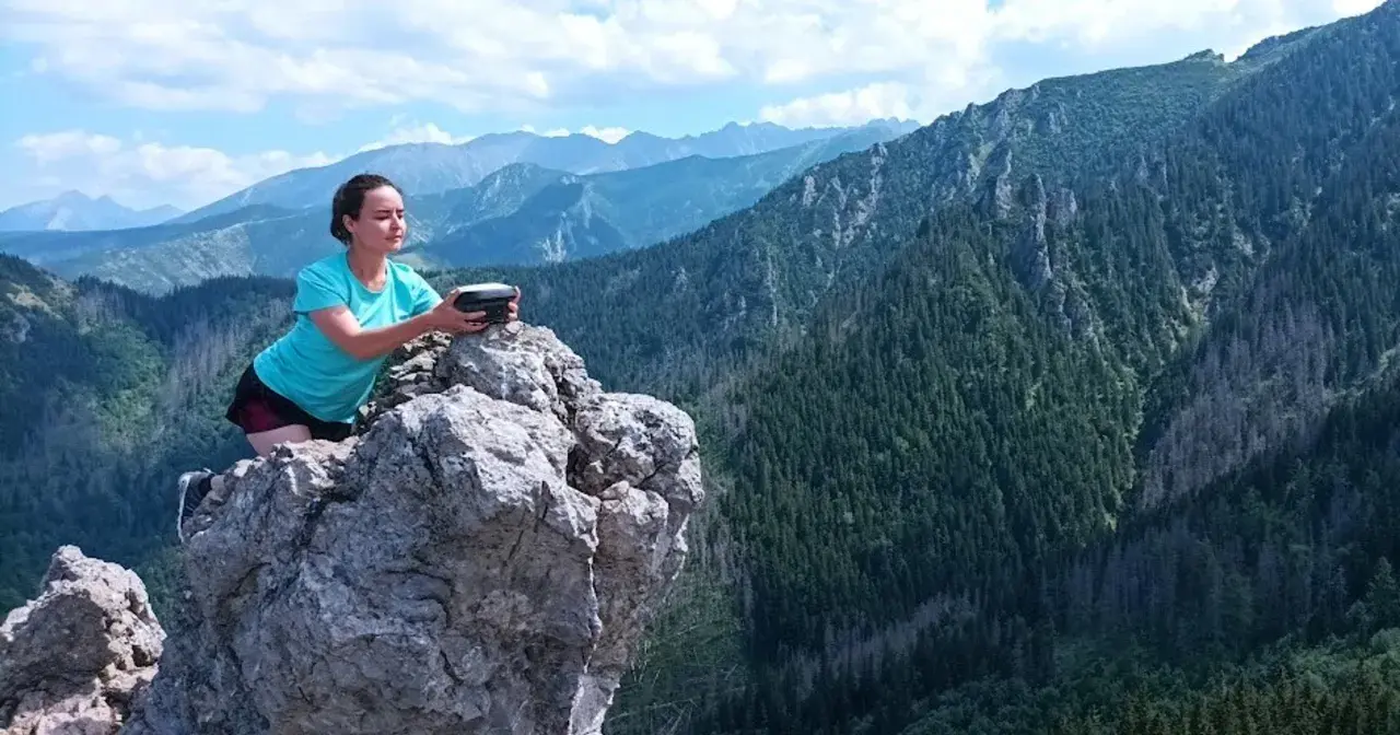 Kobieta na skale z urządzeniem w rękach, podziwia rozległą panoramę górską. Widok zapiera dech w piersiach, to prawdziwa przełęcz w tatrach wysokich.