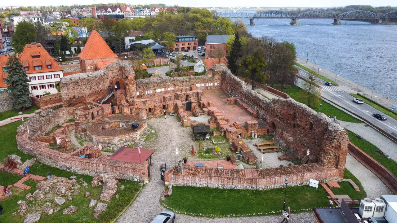 Ruiny zamku bierzgłowskiego z cegły, z widokiem na Wisłę i most.