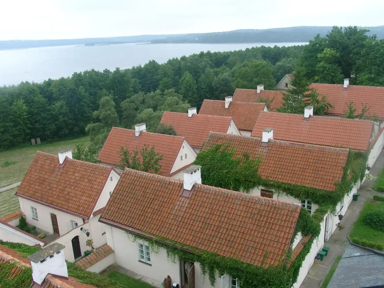 Urokliwe, pokryte czerwonymi dachówkami domy w Sejnach, otoczone zielenią, z widokiem na jezioro. Atrakcje regionu.