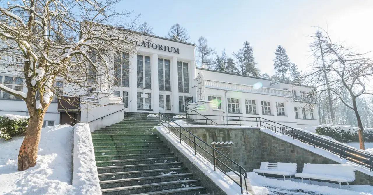 Zimowy dzień w Szczawnicy. Biały budynek sanatorium z napisem "Sanatorium" i schody pokryte śniegiem. Idealne miejsce na relaks w termach.