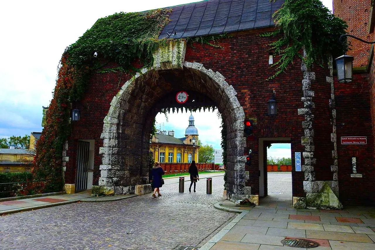 Brama wjazdowa na Wawel, porośnięta bluszczem, zaprasza do zwiedzania. Kamienna konstrukcja i ceglane mury tworzą historyczny klimat.