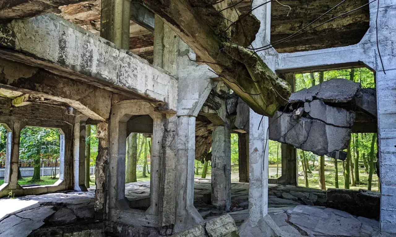 Ruiny koszar na Westerplatte podczas zwiedzania. Zniszczone betonowe konstrukcje i widok na drzewa.
