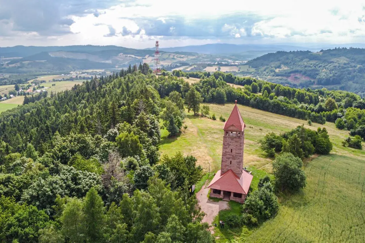 Kamienna wieża widokowa na wzgórzu, otoczona lasami i polami. Jedna z wielu wież widokowych na Dolnym Śląsku, oferująca piękne krajobrazy.
