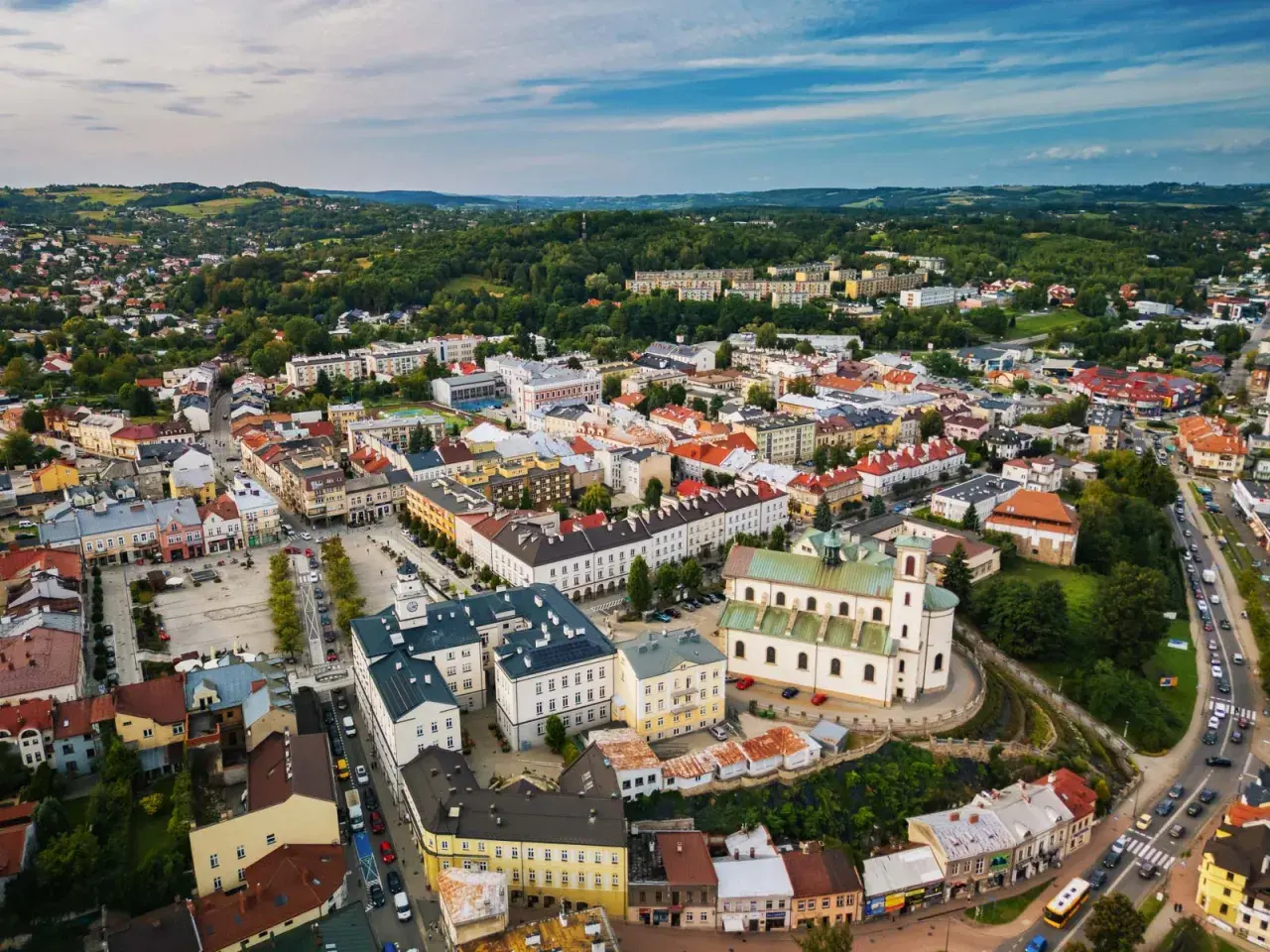 Urokliwe miasto w dolinie ropy, z dominującą białą bazyliką i kolorowymi kamienicami, otoczone zielonymi wzgórzami.