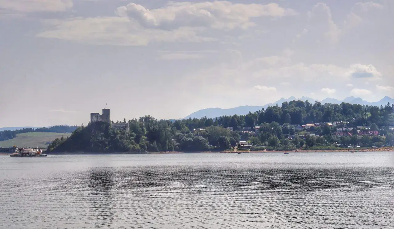 Zamek w Niedzicy góruje nad spokojnym zalewem czorsztyńskim. W oddali widać góry i malowniczą wioskę.