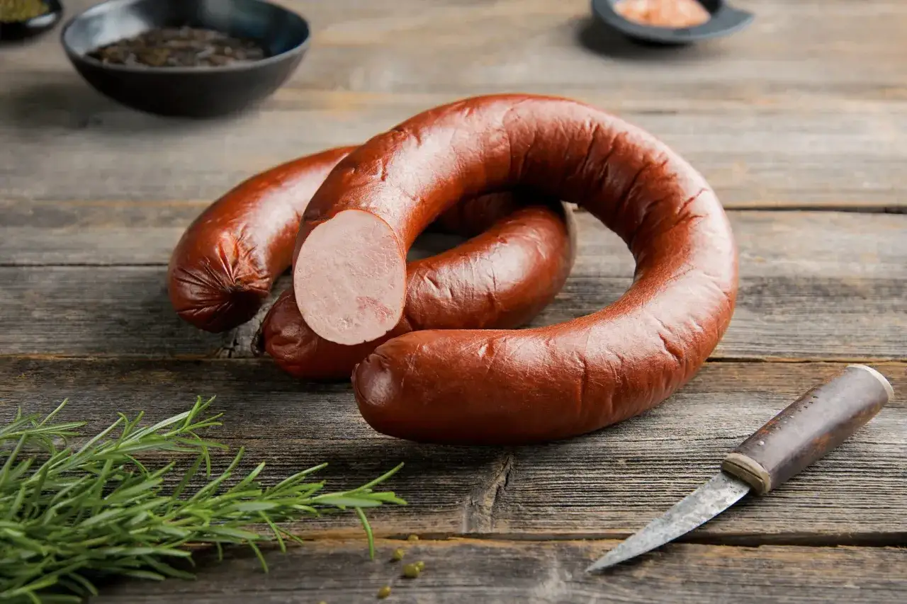 Kiełbasa lisiecka w kształcie podkowy, obok gałązka rozmarynu i nóż.