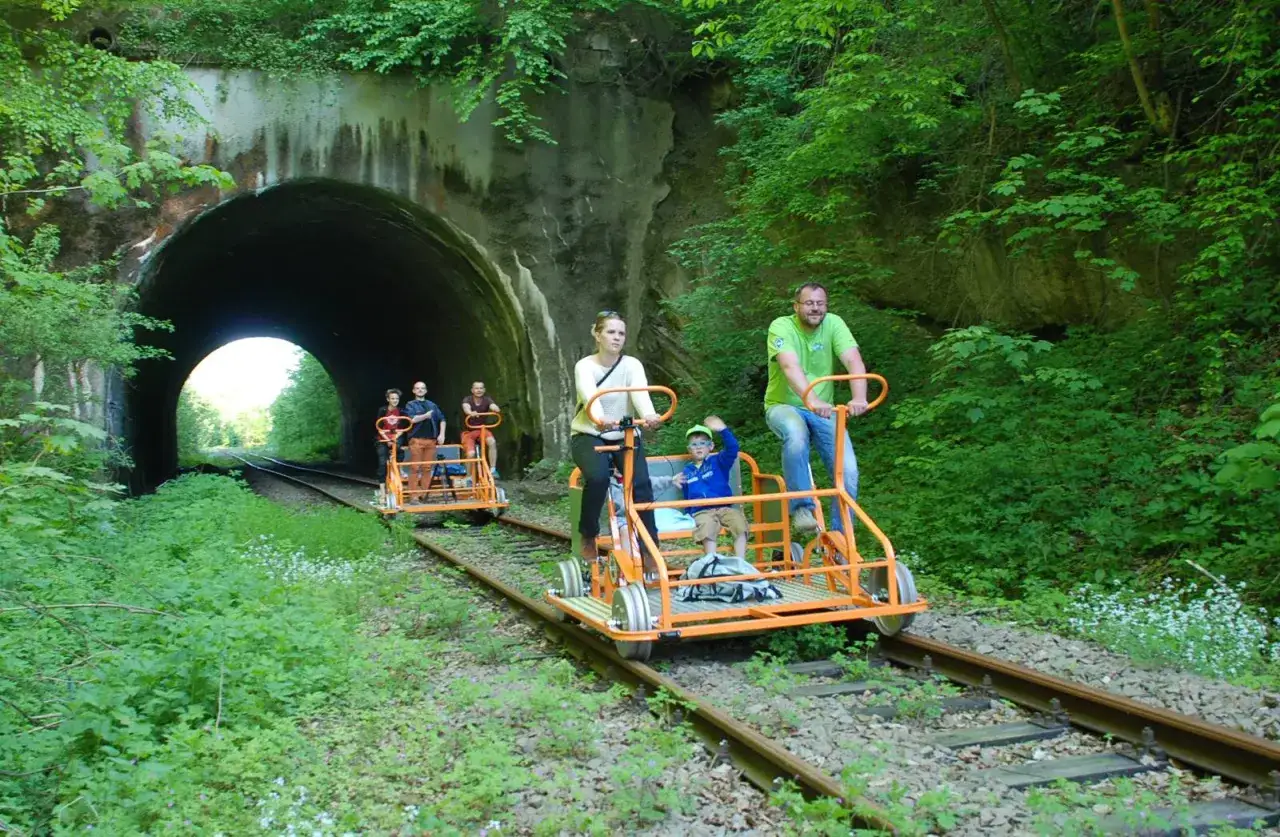 Rodzina na drezynach w Bieszczadach, przejeżdża obok tunelu kolejowego otoczonego bujną zielenią.