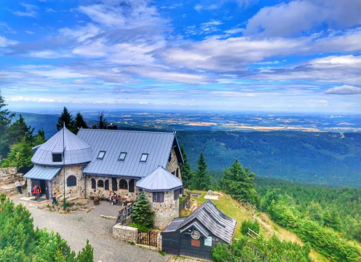 Kamienny schron turystyczny na szlaku w Górach Izerskich. Rozległa panorama krajobrazu pod błękitnym niebem.