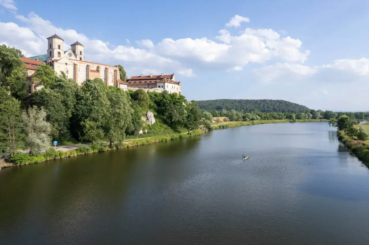 Tyniec, najstarszy klasztor w Polsce, majestatycznie wznosi się nad Wisłą. Dwa kajakarzy płyną spokojnie po rzece.