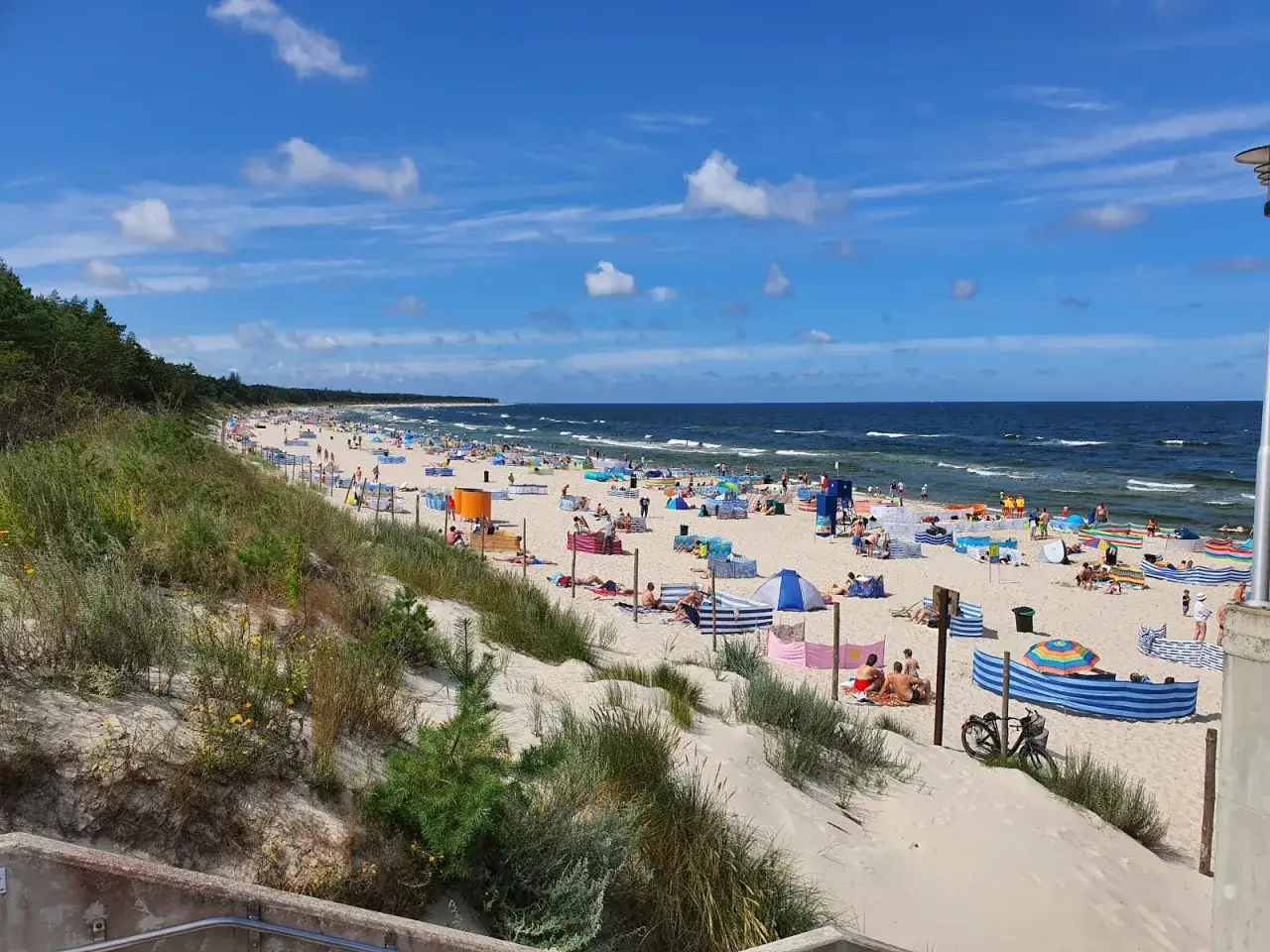 Grzybowo nadmorska: zejście na plażę pełną kolorowych parawanów i wypoczywających ludzi.