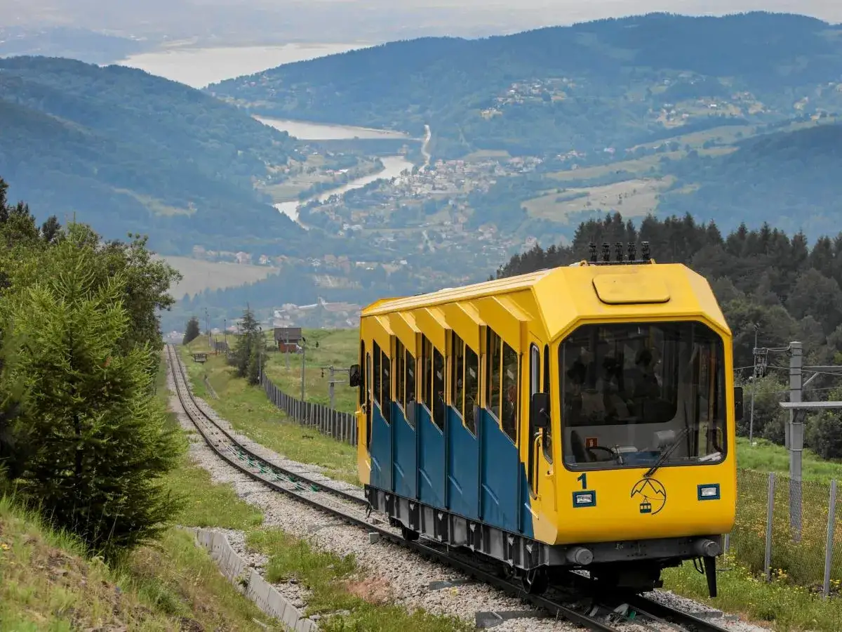 Kolejka na górę Żar, oferująca wspaniałe widoki i atrakcje, wjeżdża po torach wśród zieleni.