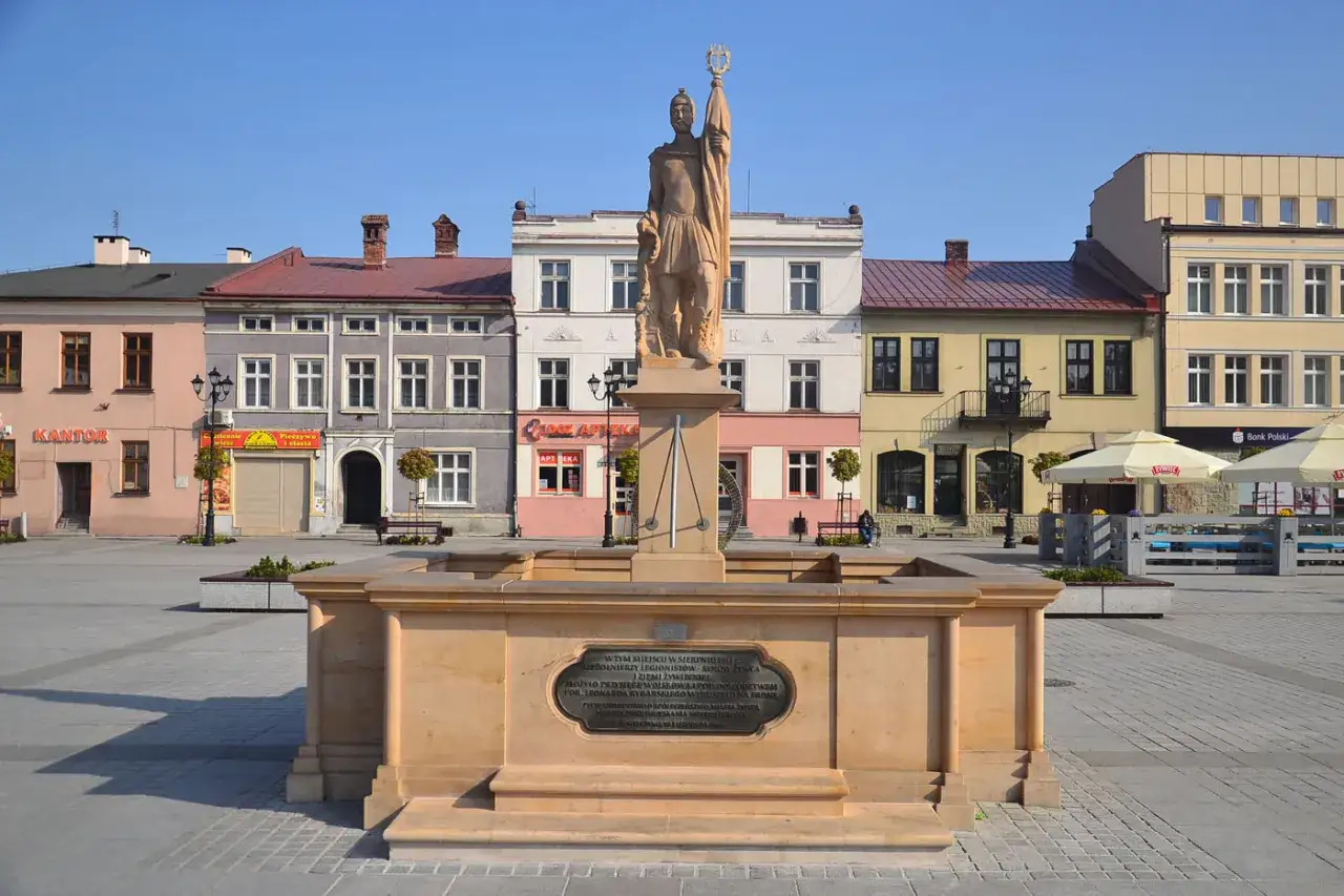 Pomnik na żywiec rynku, z żołnierzem na cokole, otoczony kolorowymi kamienicami i placem.