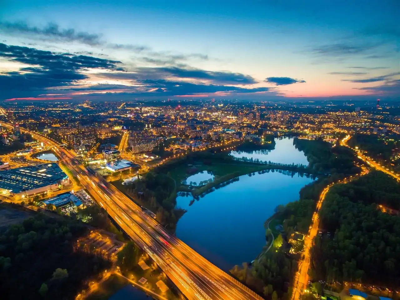 Widok z lotu ptaka na miasto nocą, z oświetloną autostradą i trzema stawami odbijającymi światła.
