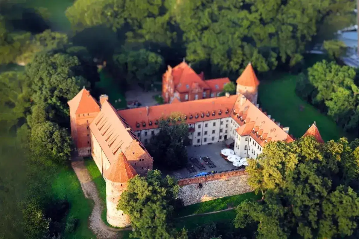 Zamek w Bytowie, otoczony zielenią, z czerwonymi dachami i kamiennymi murami, wygląda jak z bajki.
