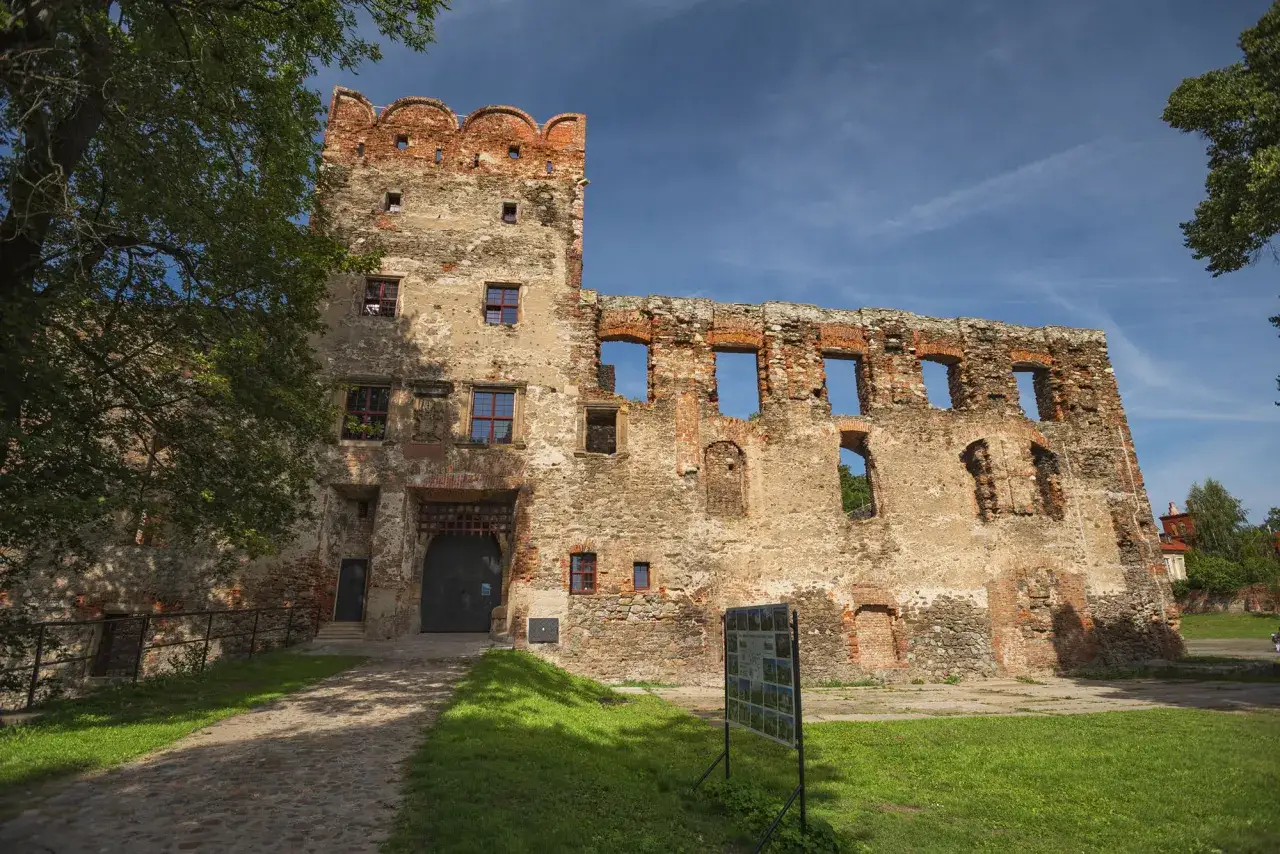 Zamek w Ząbkowicach Śląskich, ruiny zamku z ceglanymi detalami i kamiennymi murami, pod błękitnym niebem.