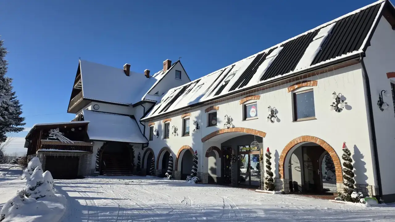 Idealne miejsce, gdzie na ferie zimowe: biały budynek z arkadami, ośnieżone dachy i choinki w czapkach Mikołaja.