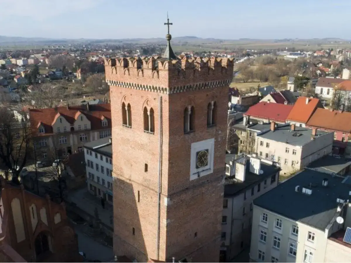Krzywa wieża w Polsce, ceglana, z zegarem i blankami, góruje nad miastem.