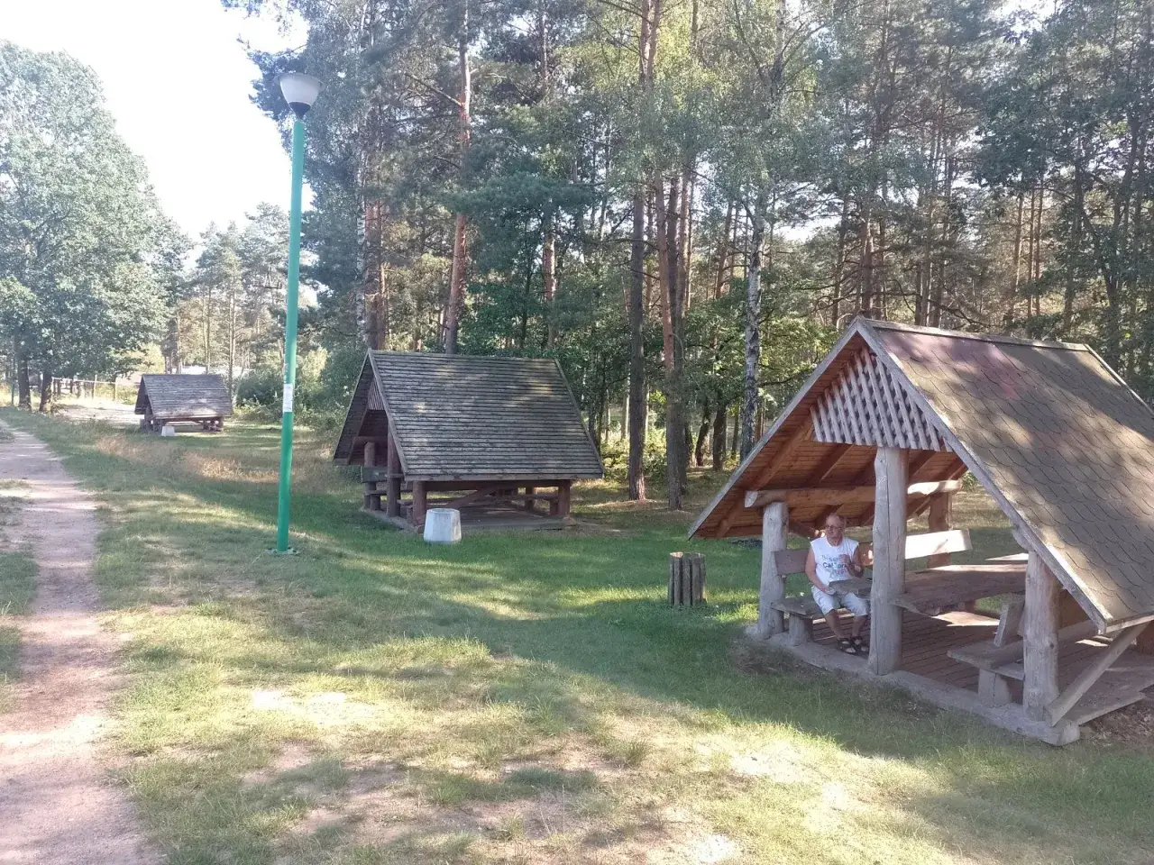 Wypoczynek nad zalewem zielona. Drewniane altany w lesie, jedna z nich zajęta przez osobę.