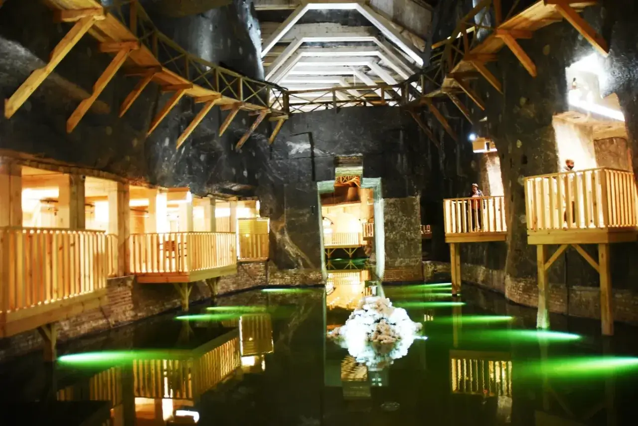 Wnętrze kopalni soli w Wieliczce. Drewniane pomosty i balustrady nad zieloną wodą, oświetloną od dołu. Stała, przyjemna temperatura w kopalni wieliczka.