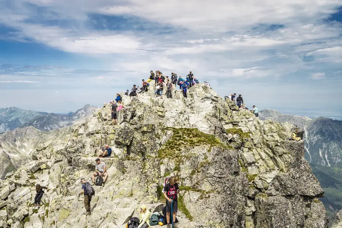 Tłum turystów na skalistym szczycie, najwyższy szczyt w Polsce, Rysy, podziwia panoramę Tatr.