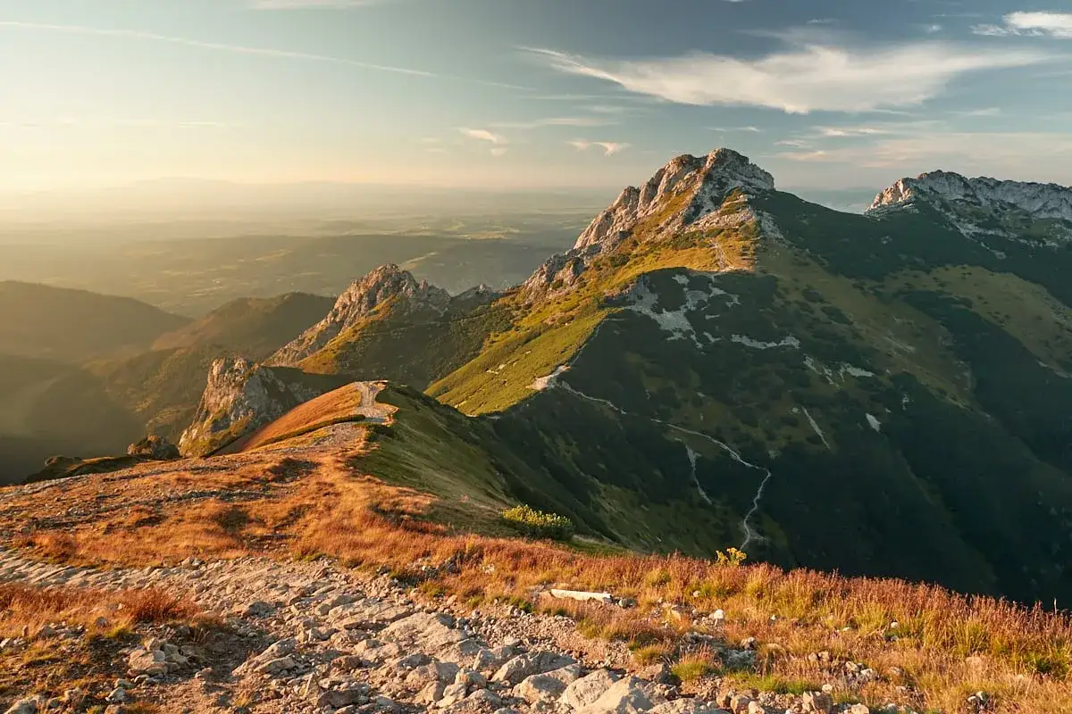 Słoneczny szlak na Giewont w Tatrach. Kręta ścieżka wije się pośród zielonych zboczy i skalistych grani, prowadząc ku majestatycznym szczytom.
