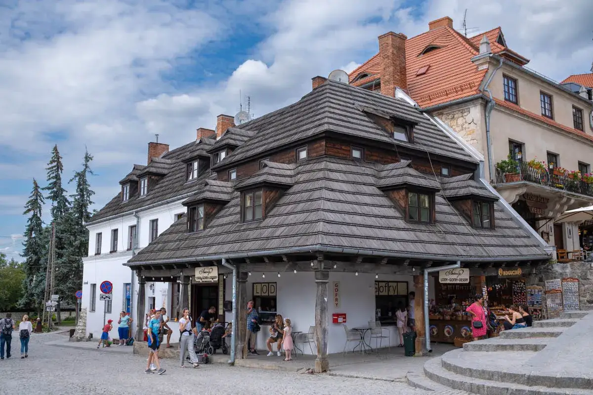 Tętniący życiem rynek w Kazimierzu Dolnym. Ludzie spacerują, kupują lody i gofry, podziwiając zabytkową architekturę.