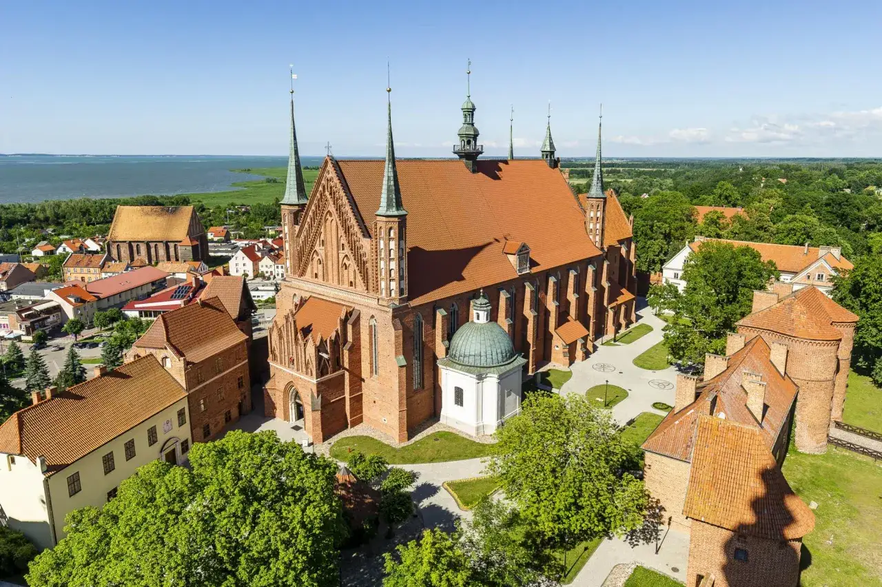 Zamek Frombork z katedrą i wieżami, otoczony zielenią i wodą.