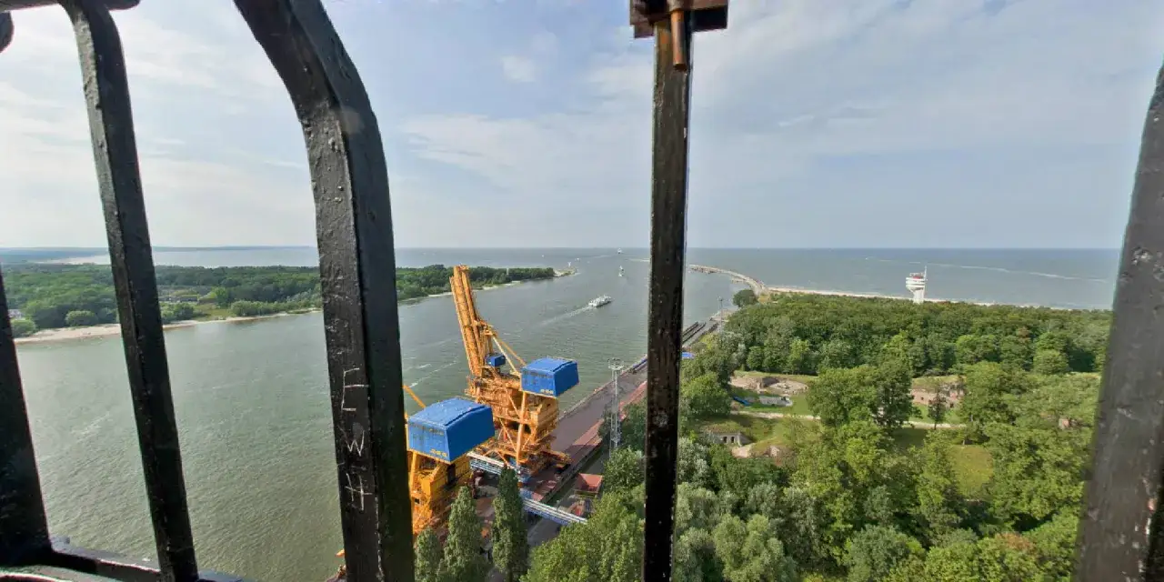 Widok z najwyższej latarni morskiej w Polsce na port, morze i zielone wybrzeże. Widać dźwig portowy i statki.